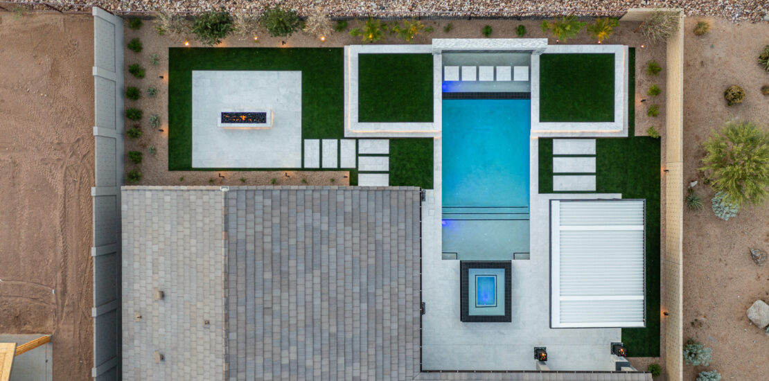 An aerial view of a modern backyard design featuring a rectangular swimming pool, surrounded by green turf and stone pathways.