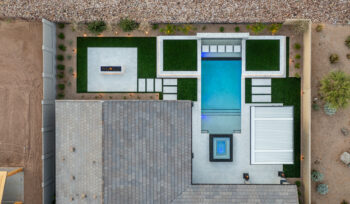 An aerial view of a modern backyard design featuring a rectangular swimming pool, surrounded by green turf and stone pathways.