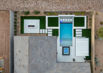 An aerial view of a modern backyard design featuring a rectangular swimming pool, surrounded by green turf and stone pathways.