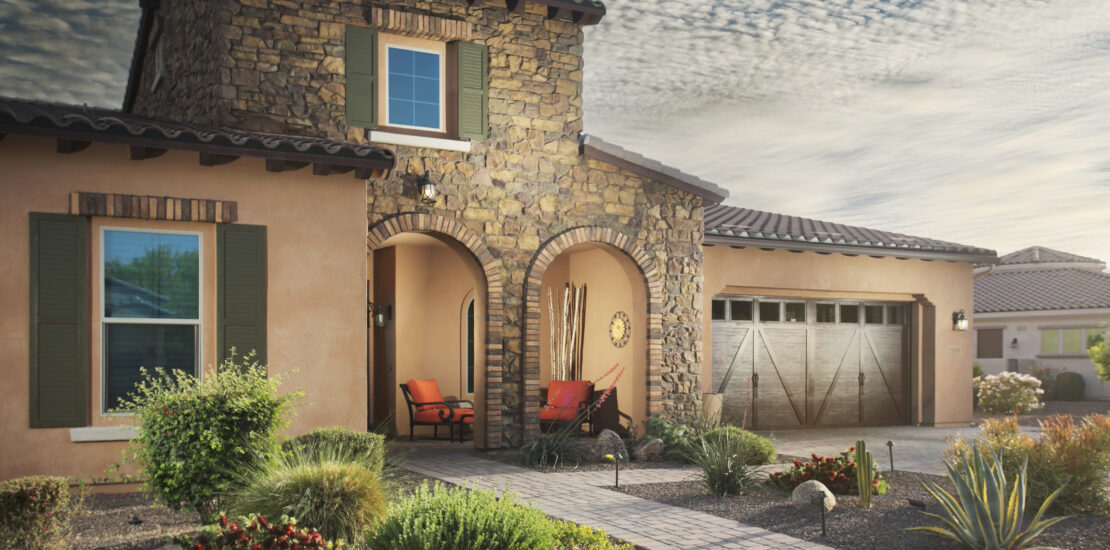 Desert landscaping with agave, shrubs, and grasses on gravel, with a stone pathway leading to a house entrance.