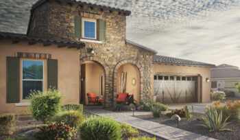 Desert landscaping with agave, shrubs, and grasses on gravel, with a stone pathway leading to a house entrance.