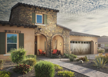 Desert landscaping with agave, shrubs, and grasses on gravel, with a stone pathway leading to a house entrance.