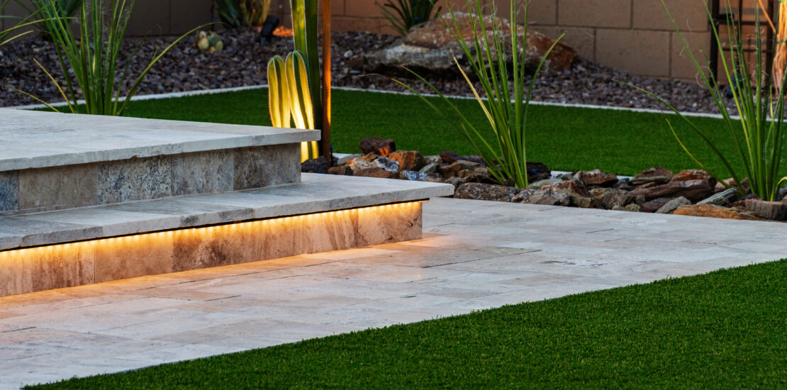 Modern Arizona backyard with illuminated stone steps, artificial grass, desert plants, and decorative rocks, creating a stylish and low-maintenance outdoor space