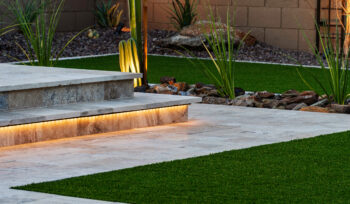 Modern Arizona backyard with illuminated stone steps, artificial grass, desert plants, and decorative rocks, creating a stylish and low-maintenance outdoor space