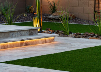 Modern Arizona backyard with illuminated stone steps, artificial grass, desert plants, and decorative rocks, creating a stylish and low-maintenance outdoor space